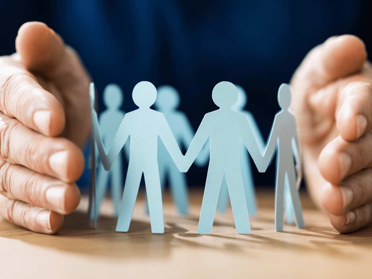 Hands protecting paper people representing safety and unity